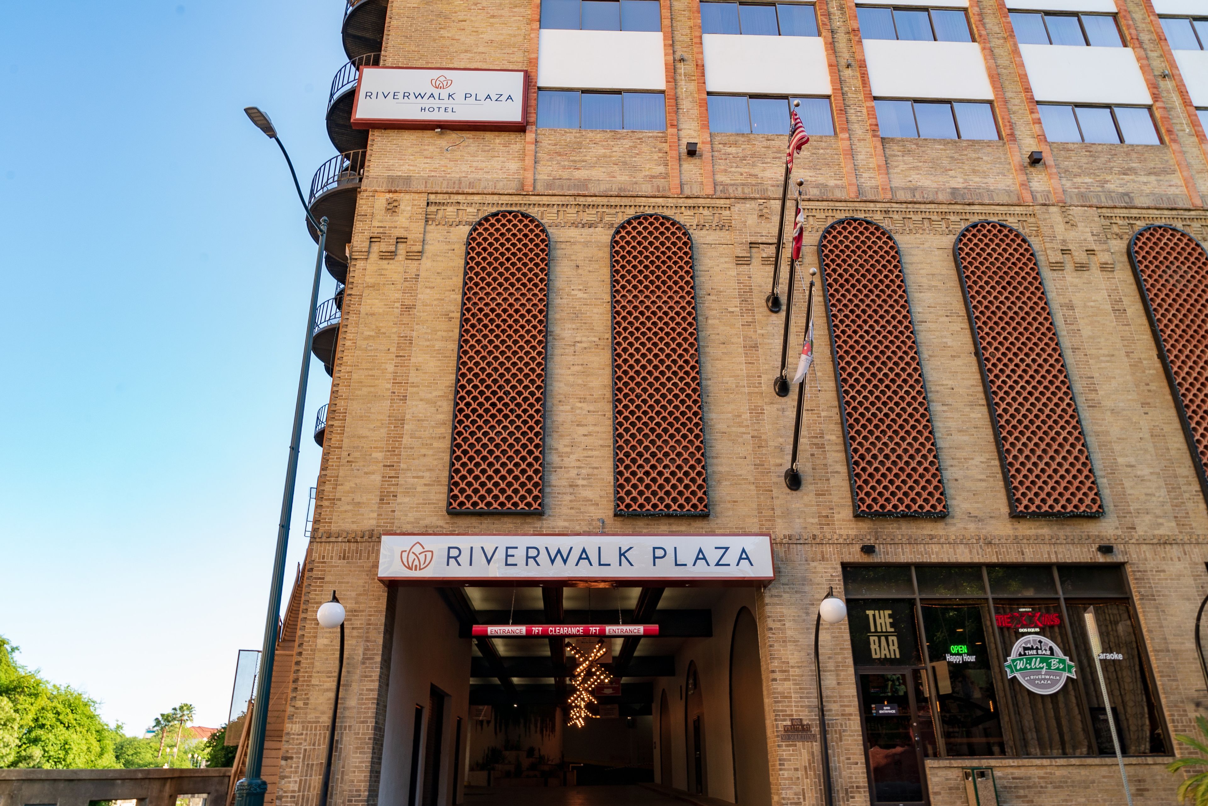 Exterior del Hotel Riverwalk Plaza, con entrada despejada, un bar y un cartel que indica el nombre del hotel.