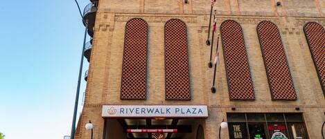 Exterior del Hotel Riverwalk Plaza, con entrada despejada, un bar y un cartel que indica el nombre del hotel.