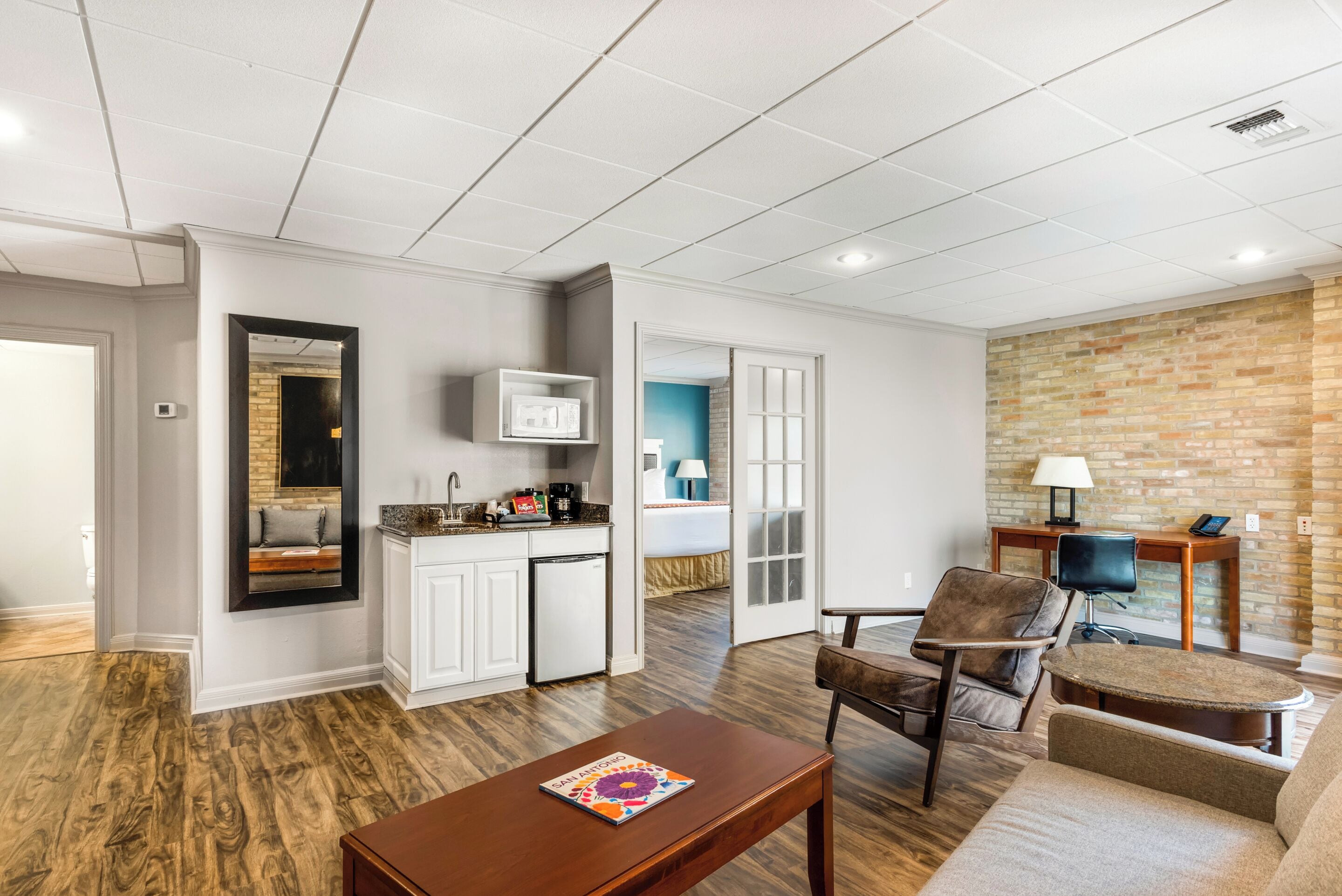 A modern living room with a wooden floor, a coffee table, a sofa, and a dining area with a kitchen in the background.