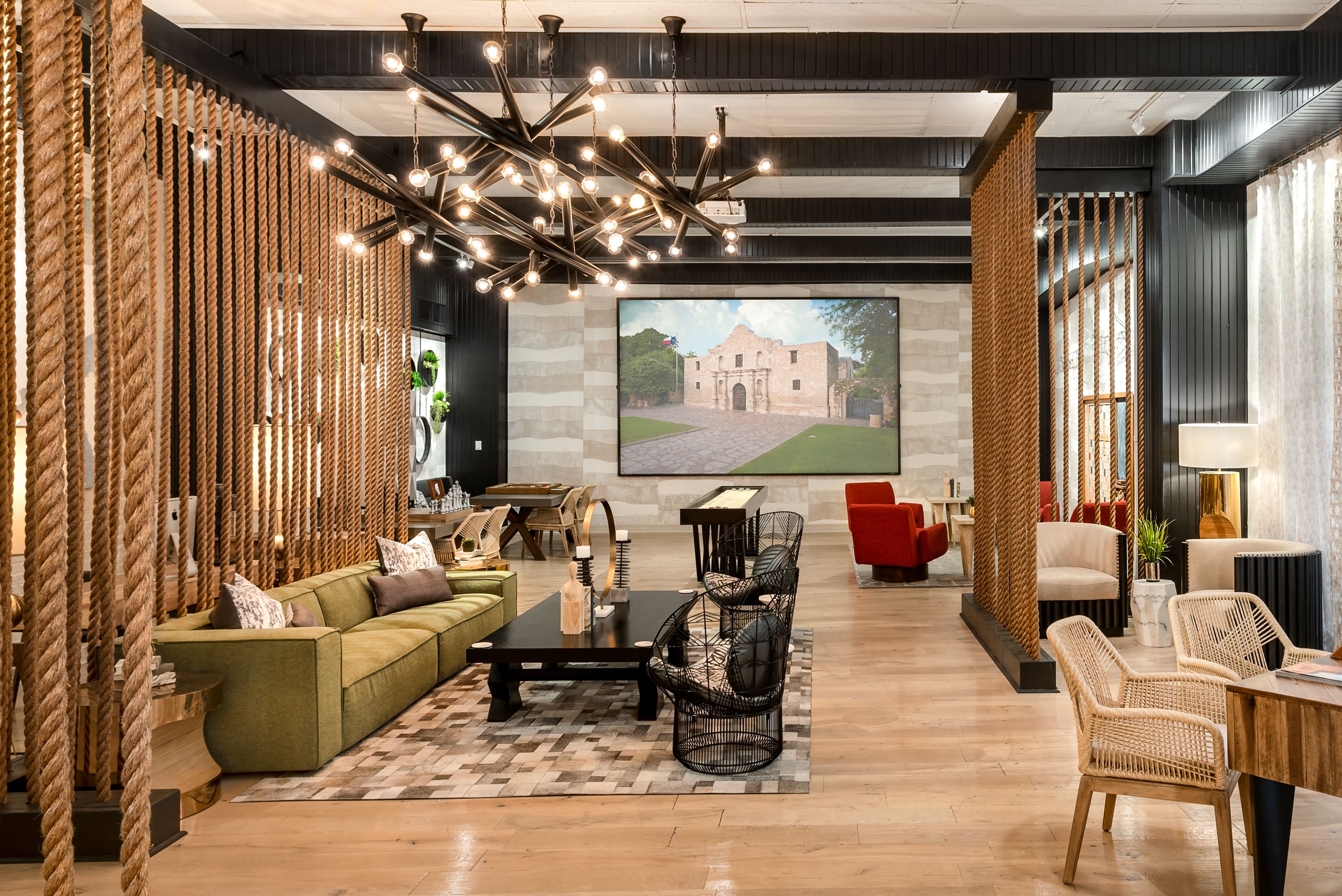 Una sala de estar moderna con un sofá modular, una mesa de centro y sillones de mimbre. Una pantalla grande muestra una imagen de un edificio.