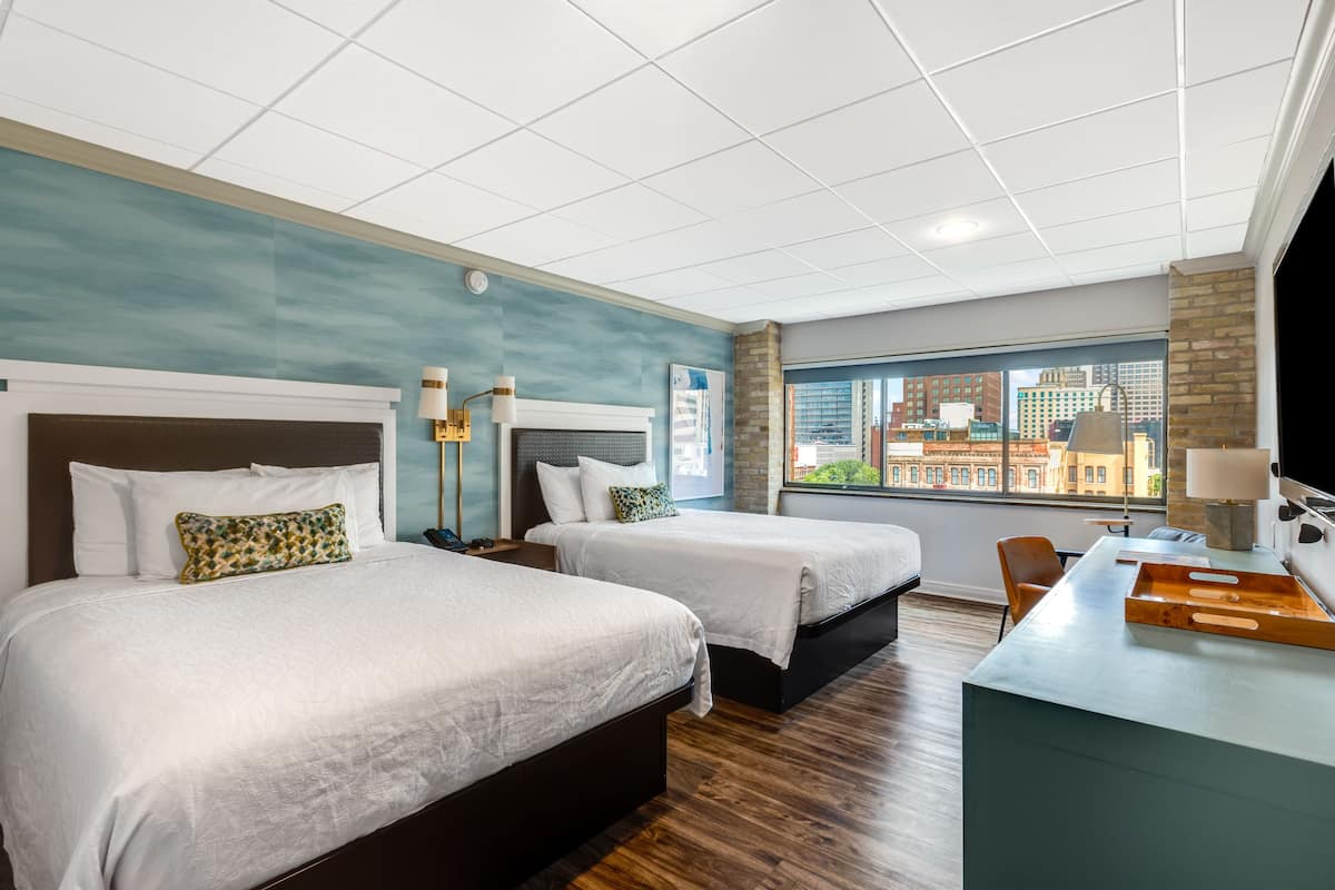 Habitación de hotel con dos camas, un escritorio y vistas a la ciudad.