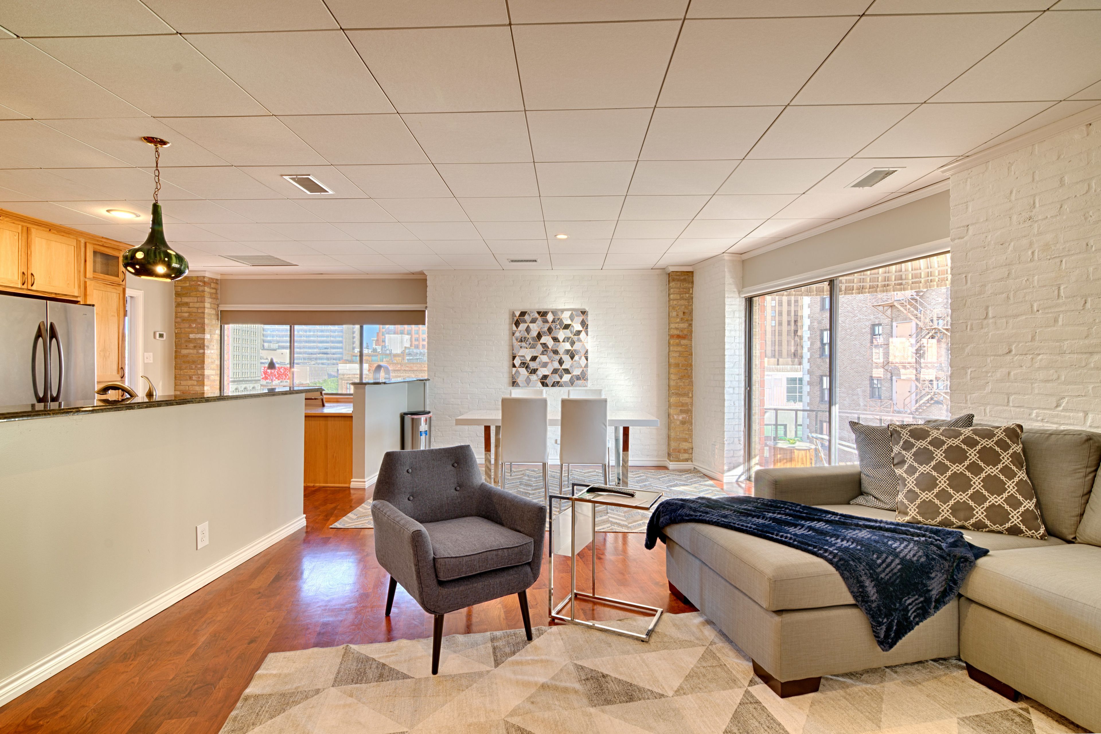 A modern living room with a sofa, armchair, and a dining area with a table and chairs.