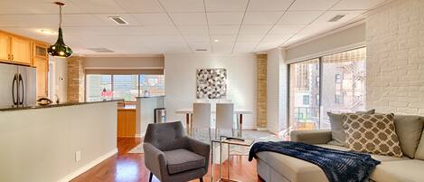 A modern living room with a sofa, armchair, and a dining area with a table and chairs.