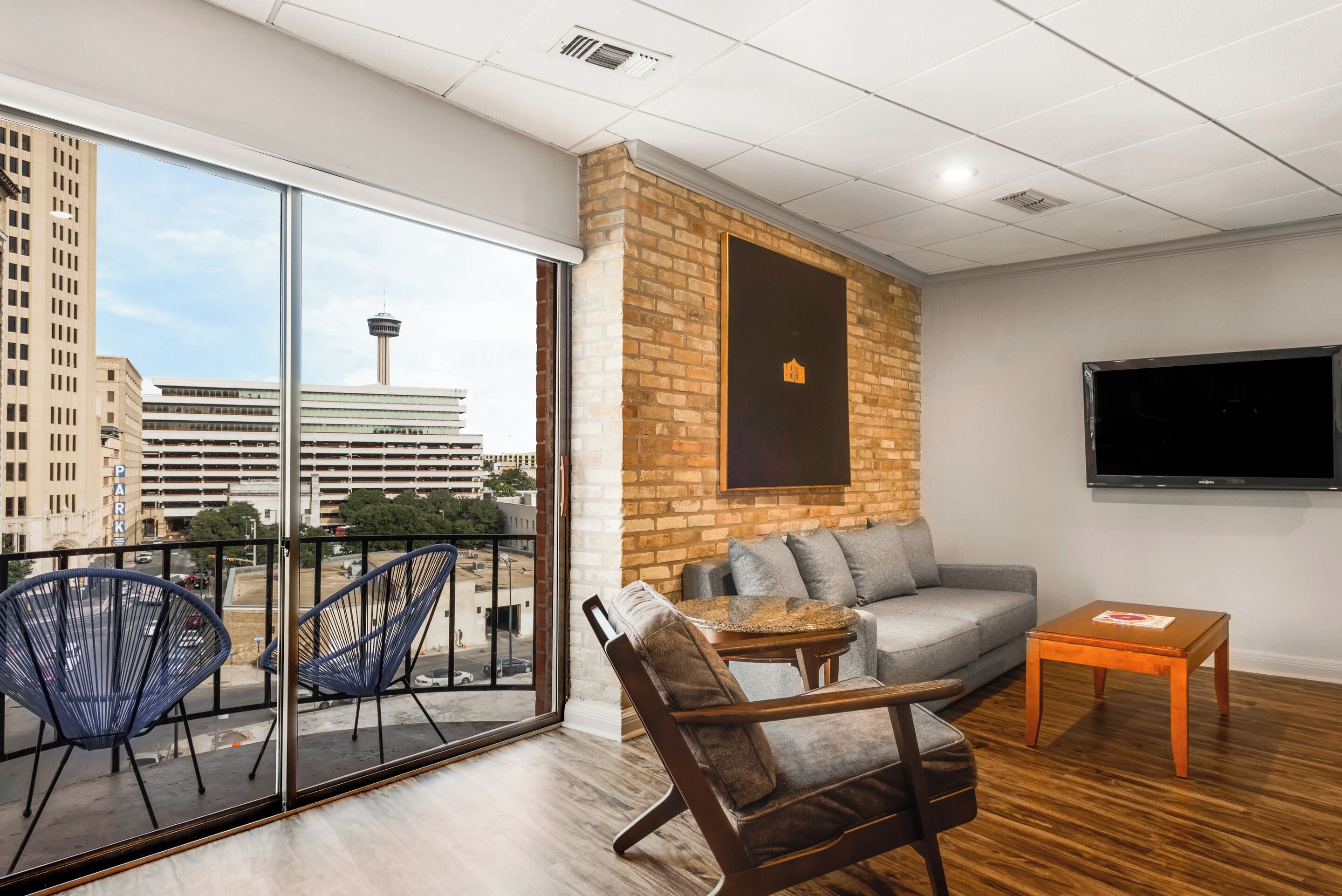 A modern living room with a sofa, armchairs, a TV, and a balcony with a city view.