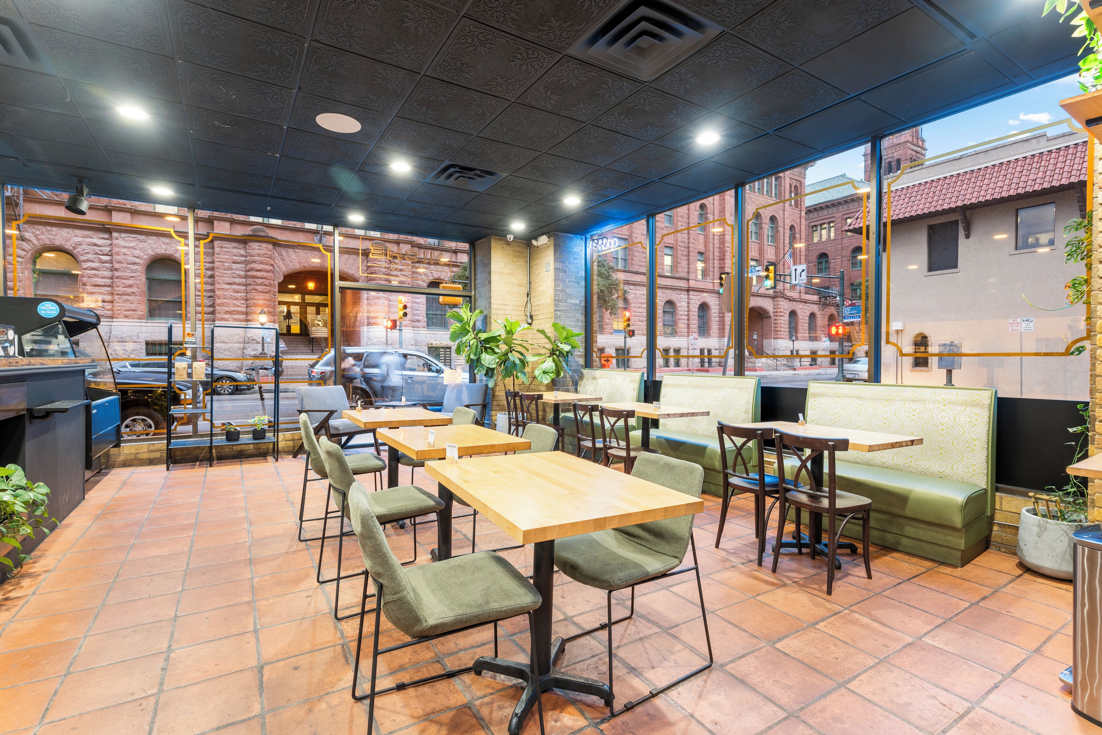 An indoor dining area with tables and chairs, large windows, and a view of the street.
