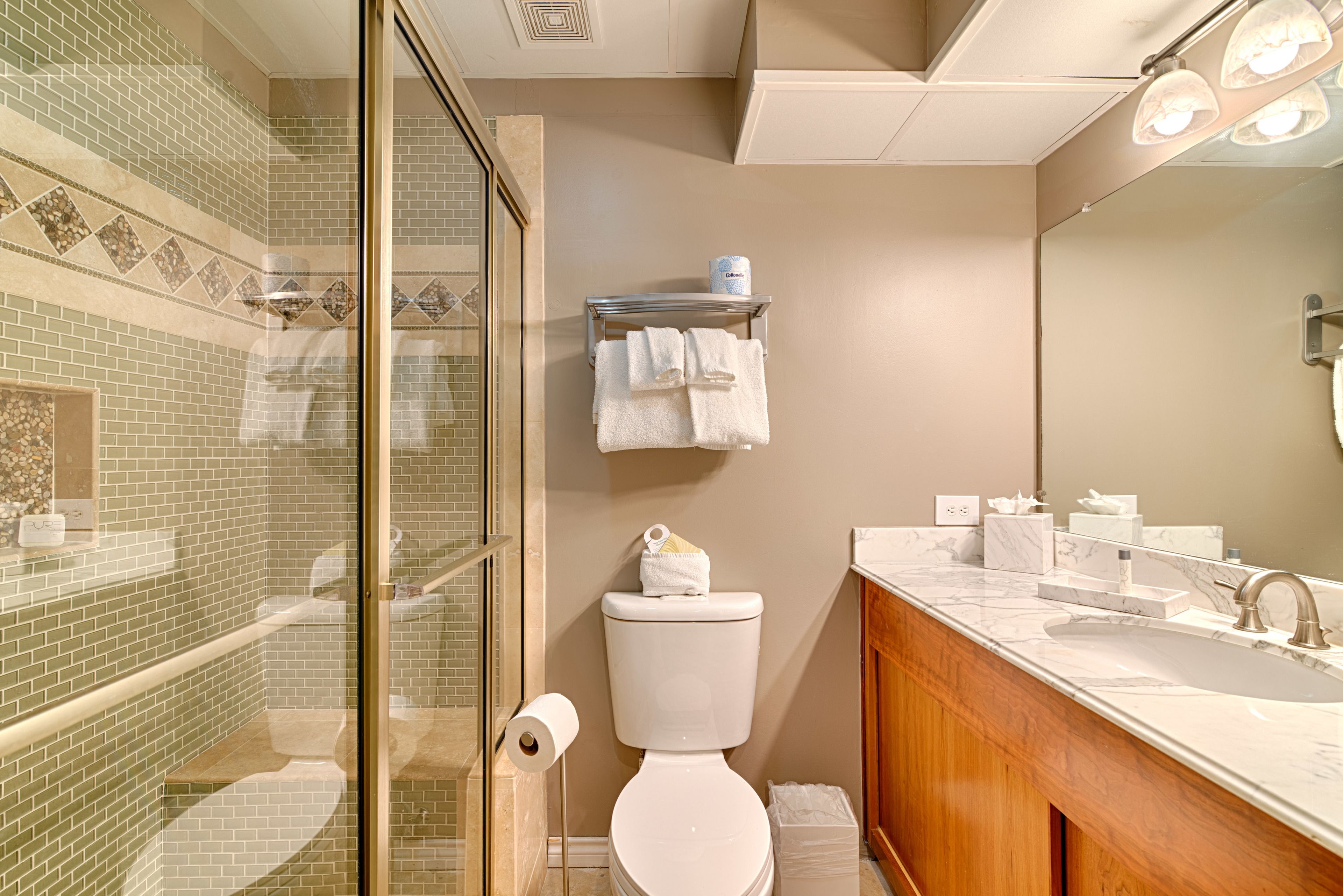 Een badkamer met een douchecabine van glas, een toilet, een wastafel met spiegel en een plank met handdoeken en toiletartikelen.