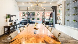 A conference room with a long wooden table, leather chairs, a modern chandelier, and a view of the street through large windows.