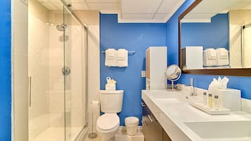Une salle de bain moderne avec une douche à parois de verre, des toilettes blanches et un grand miroir au-dessus du lavabo.