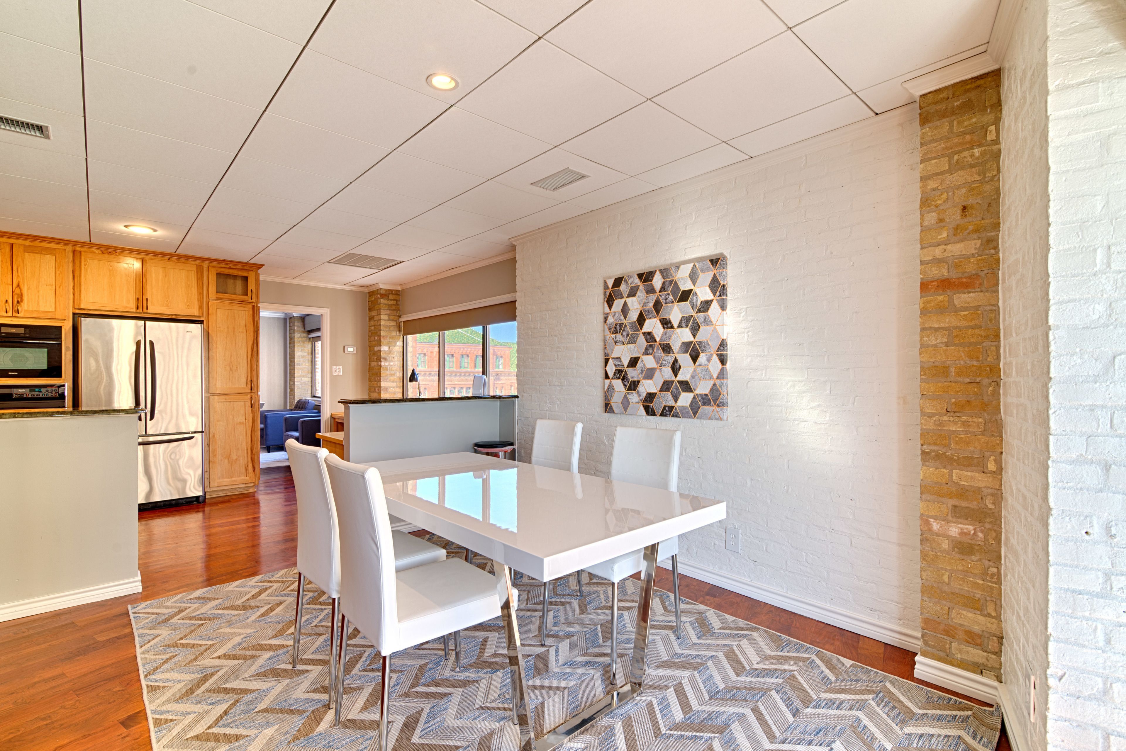 A modern kitchen with wooden cabinets, a built-in refrigerator, and a dining area with a white table and chairs.