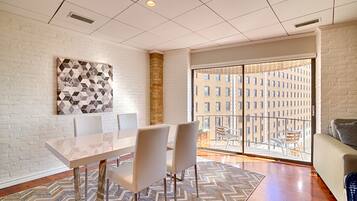 A modern dining area with a white table and chairs, a patterned wall art, and a view of a building through a glass door.