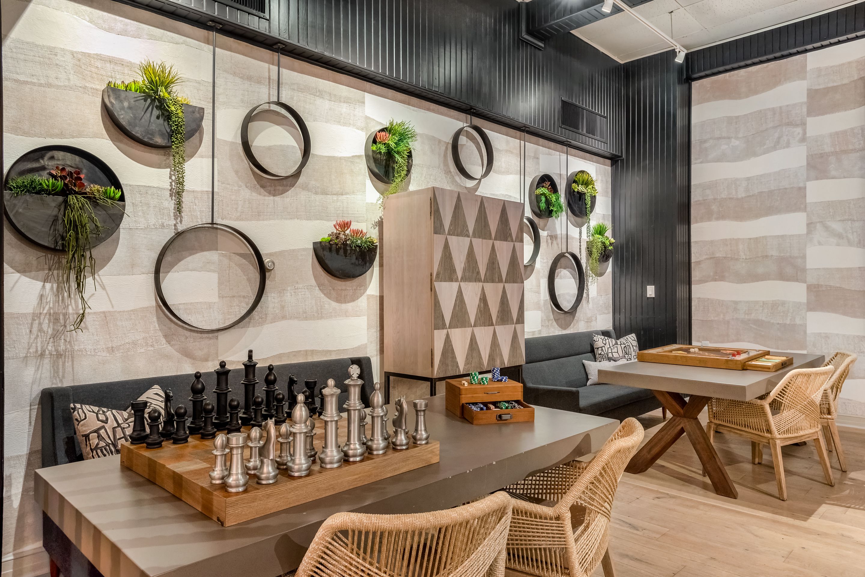 Un espace de détente moderne avec un jeu d’échecs, des fauteuils en osier et des jardinières murales de forme circulaire.