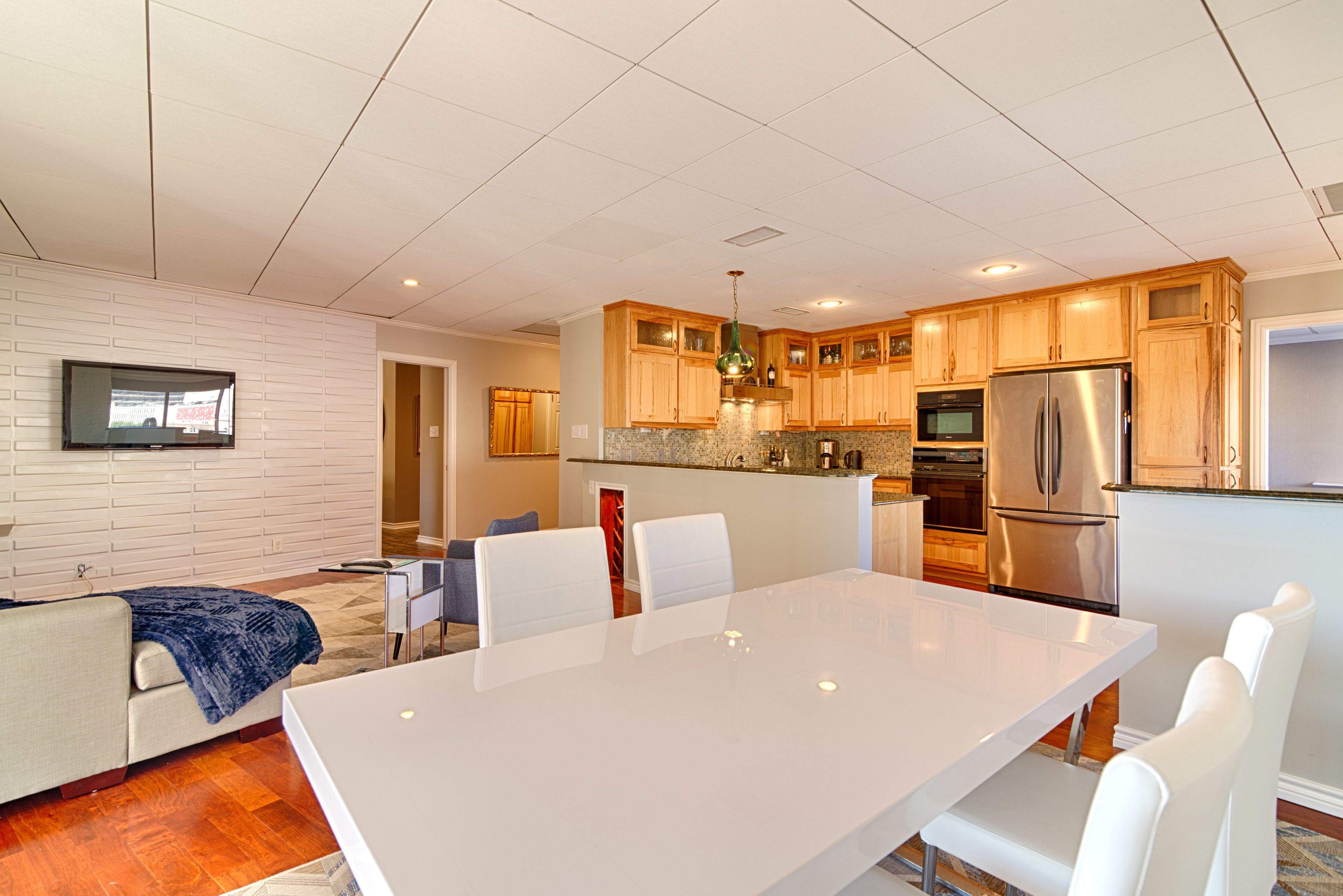 A modern kitchen with wooden cabinets, a stainless steel refrigerator, and a dining area with a white table and chairs.