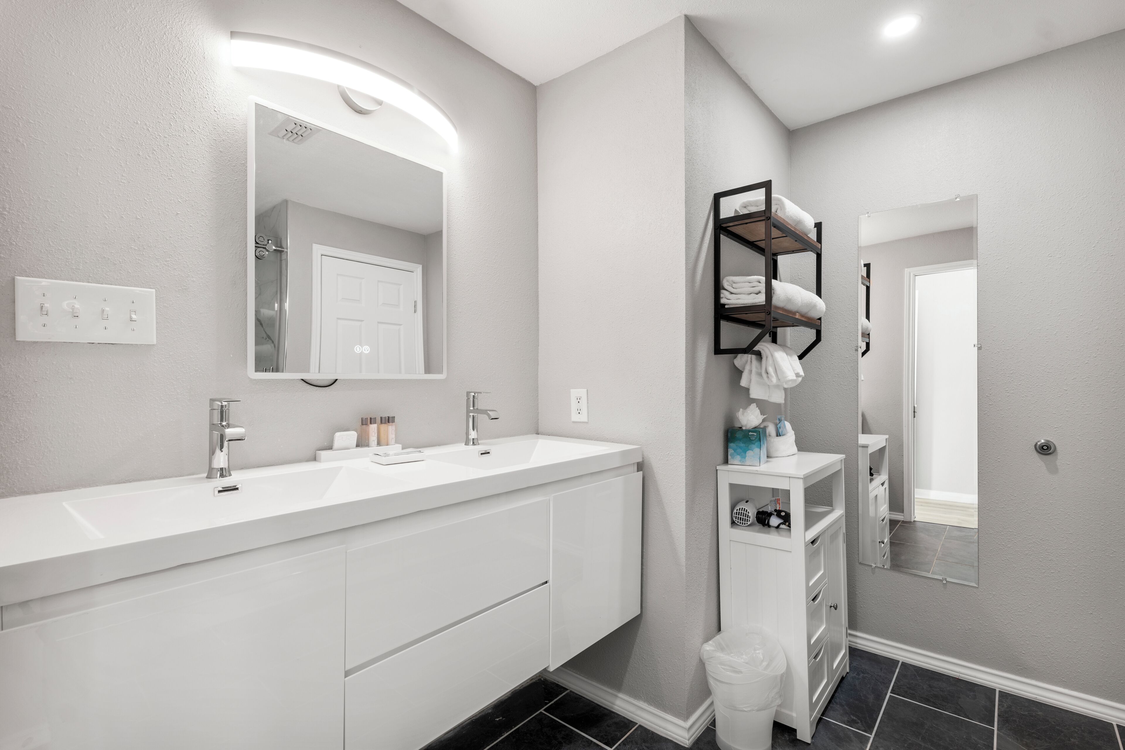 A modern bathroom with a white vanity, dual sinks, a large mirror, and a black towel rack.