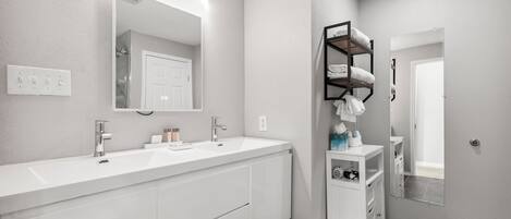 Une salle de bain moderne avec un meuble-lavabo blanc, deux vasques, un grand miroir et un porte-serviettes noir.