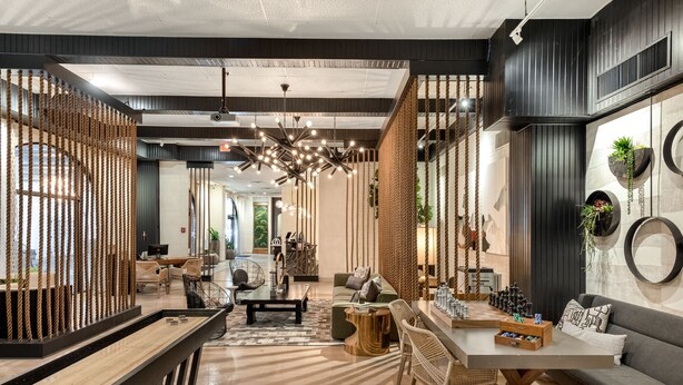 A modern interior with a wooden floor, a central seating area with a sofa and chairs, a long table, and a decorative wall with plants and circular mirrors.
