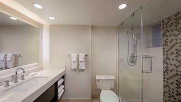 A modern bathroom with a large mirror, dual sinks, a toilet, and a glass-enclosed shower area.