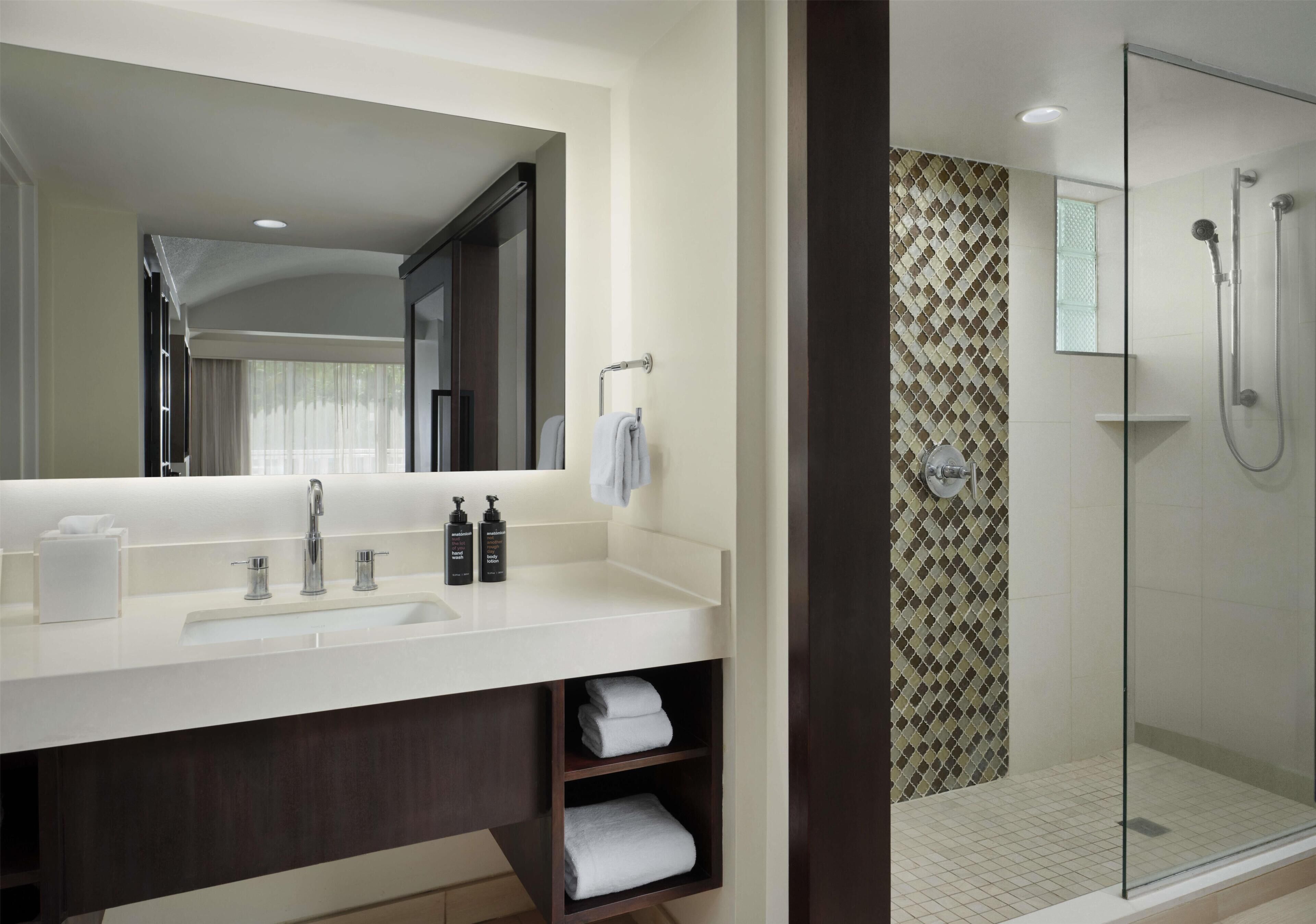 Un baño moderno con un espejo grande, un lavabo, una ducha y un perchero para toallas.