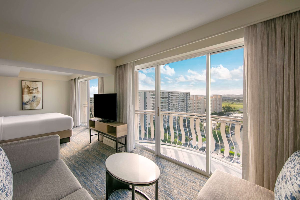 Habitación de hotel con cama, televisión, una mesita y balcón con vista a la ciudad.