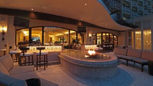 Un espace de détente moderne doté d’un foyer central, de sièges et d’un bar, le tout visible à travers une cloison en verre.