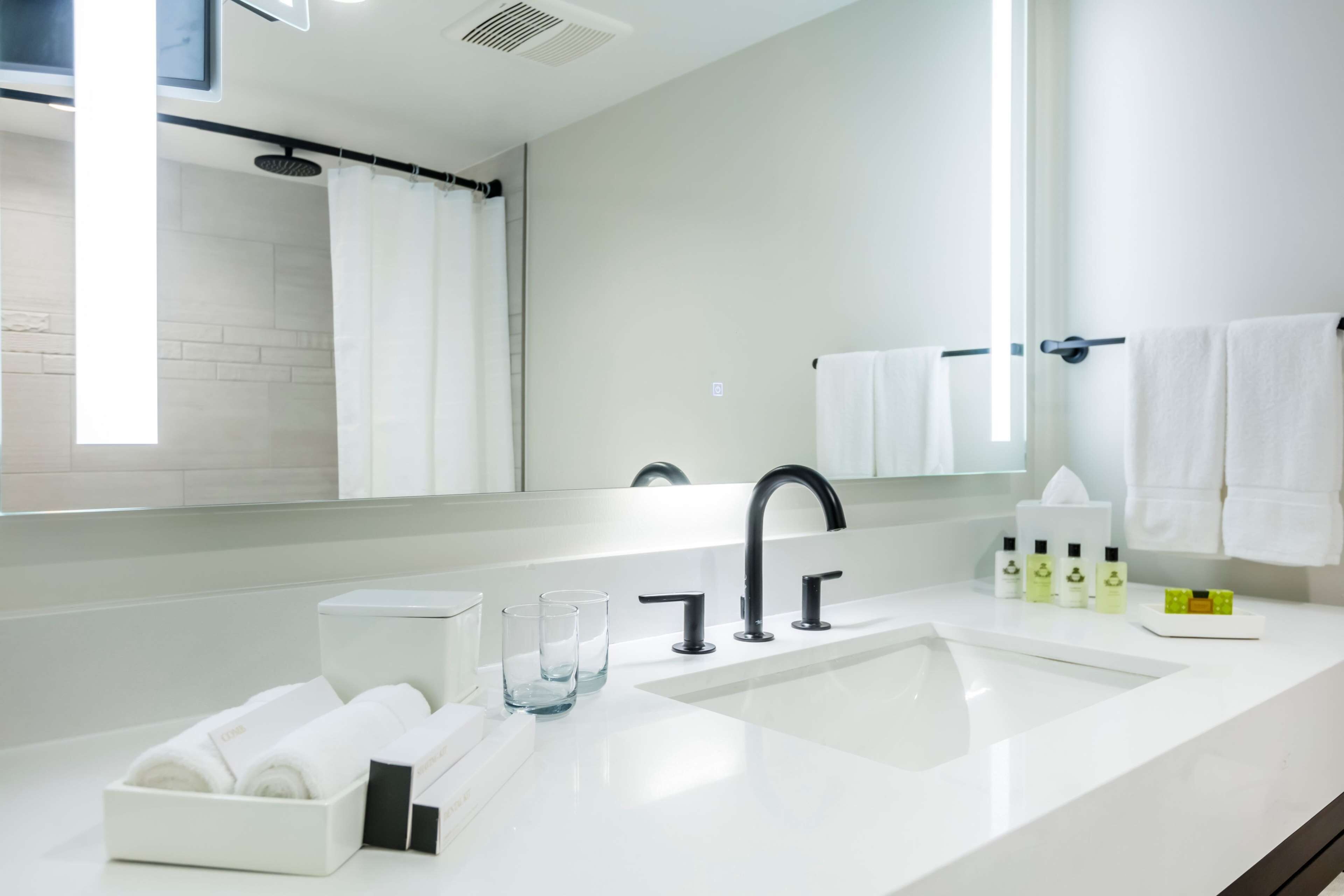 A modern bathroom with a white sink, black faucet, and a mirror above it. There are towels and toiletries on the counter.