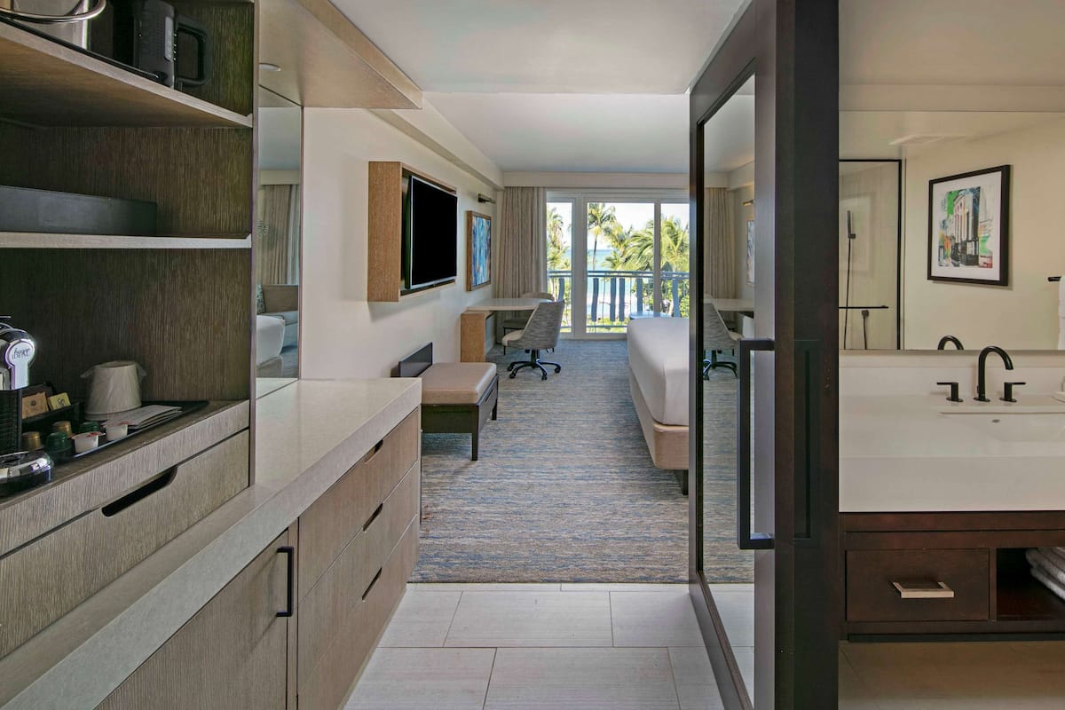 Una habitación de hotel moderna con una cama grande, un escritorio, un televisor y un baño con lavabo y espejo.