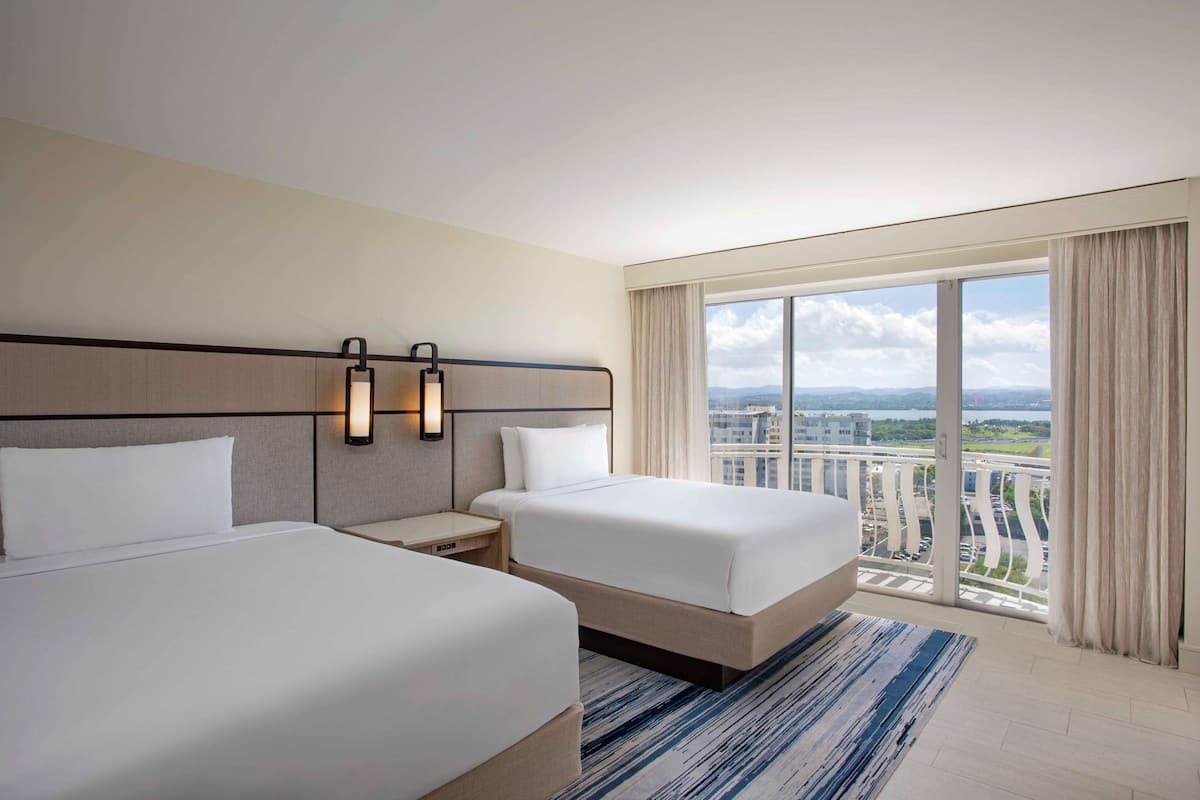 Una habitación de hotel con dos camas, un ventanal con vistas y un balcón.