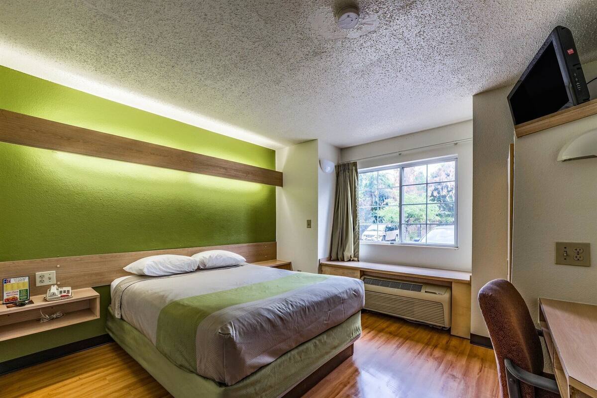 Ein Hotelzimmer mit Bett, Schreibtisch, Stuhl, Fenster mit Blick und einer Deckenleuchte.