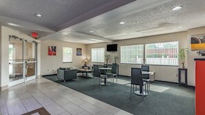 A spacious lobby with a high ceiling, recessed lighting, a reception desk, and a seating area with chairs and tables. - Motel 6 Charlotte, NC - University (Charlotte)