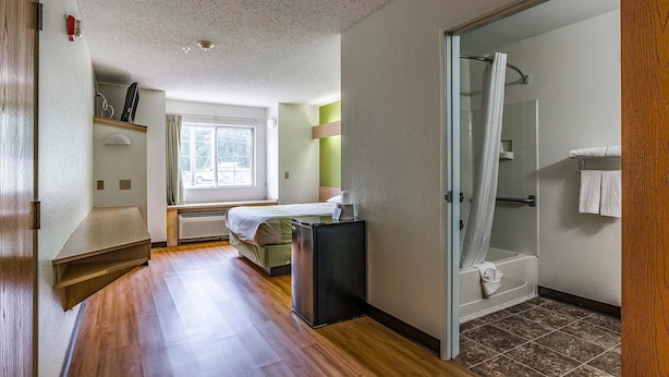 A hotel room with a wooden floor, a bed, a desk, a window, a shower, and a bathroom. - Motel 6 Charlotte, NC - University (Charlotte)