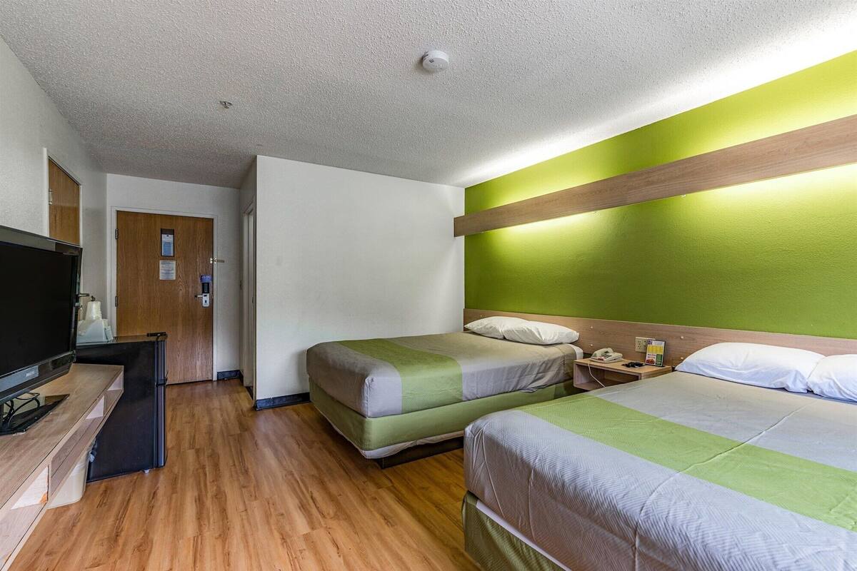 Ein Hotelzimmer mit zwei Betten, einem Fernseher, Holzboden und einer grünen Akzentwand.