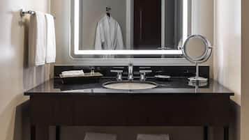 A modern bathroom with a dark wood vanity, a large mirror with integrated lighting, a round vanity mirror, and two towels on the floor.