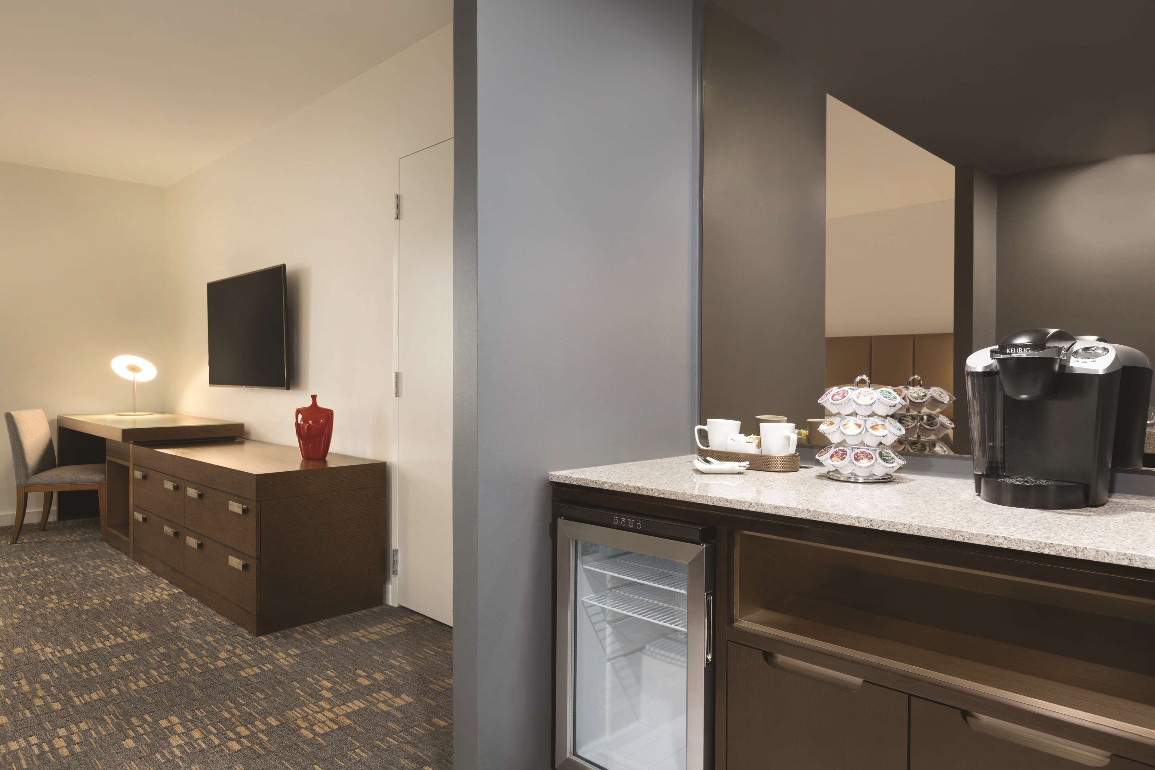 A hotel room with a kitchenette, a refrigerator, a coffee maker, and a mirror.