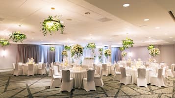 A banquet hall with round tables, white chairs, and hanging floral arrangements.