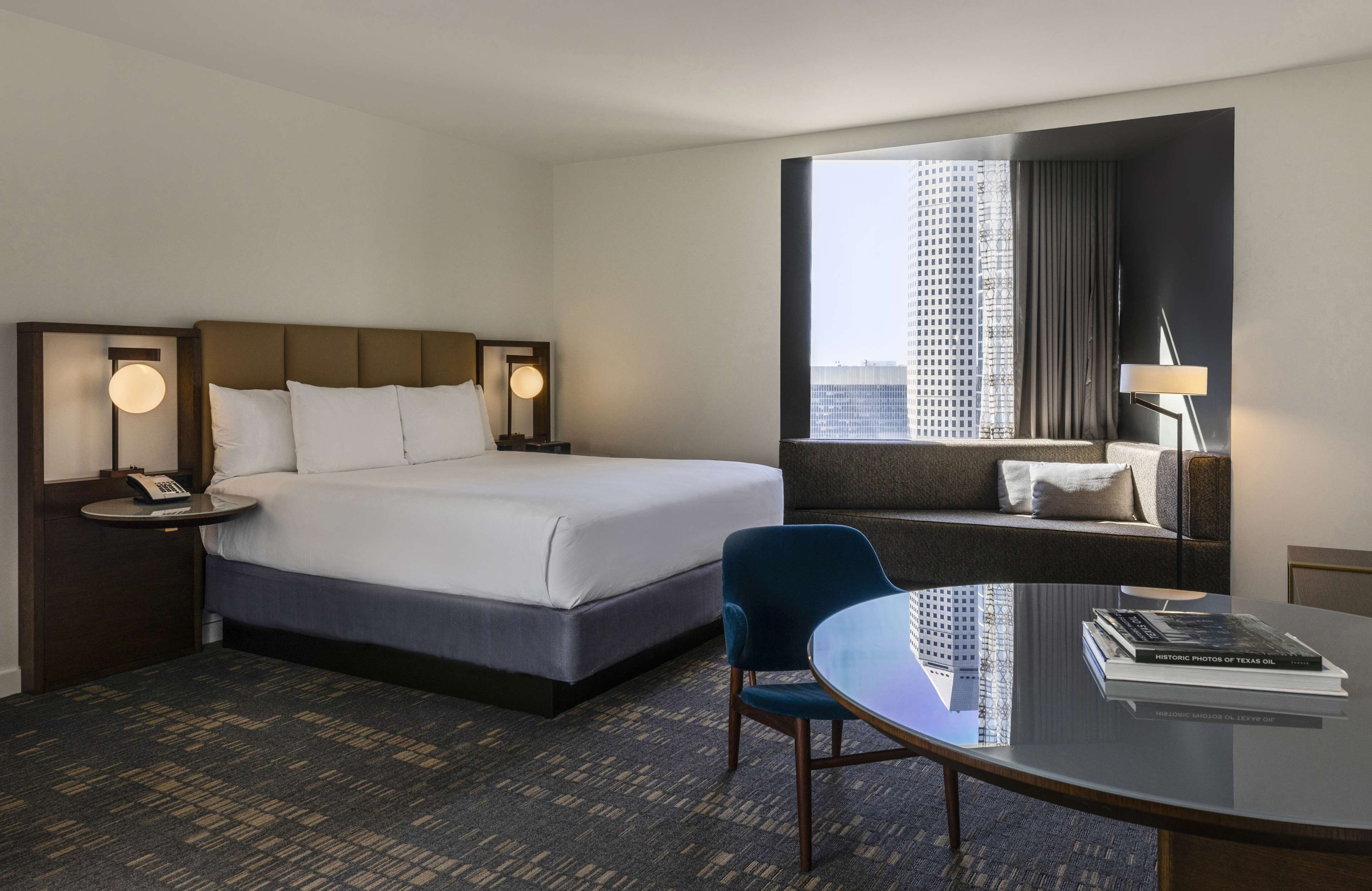 A hotel room with a large bed, a sofa, a glass table, and a view of a cityscape.