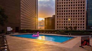 A swimming pool with lounge chairs and a flamingo float, surrounded by tall buildings and a sunset view. - Hyatt Regency Houston Downtown (Houston)