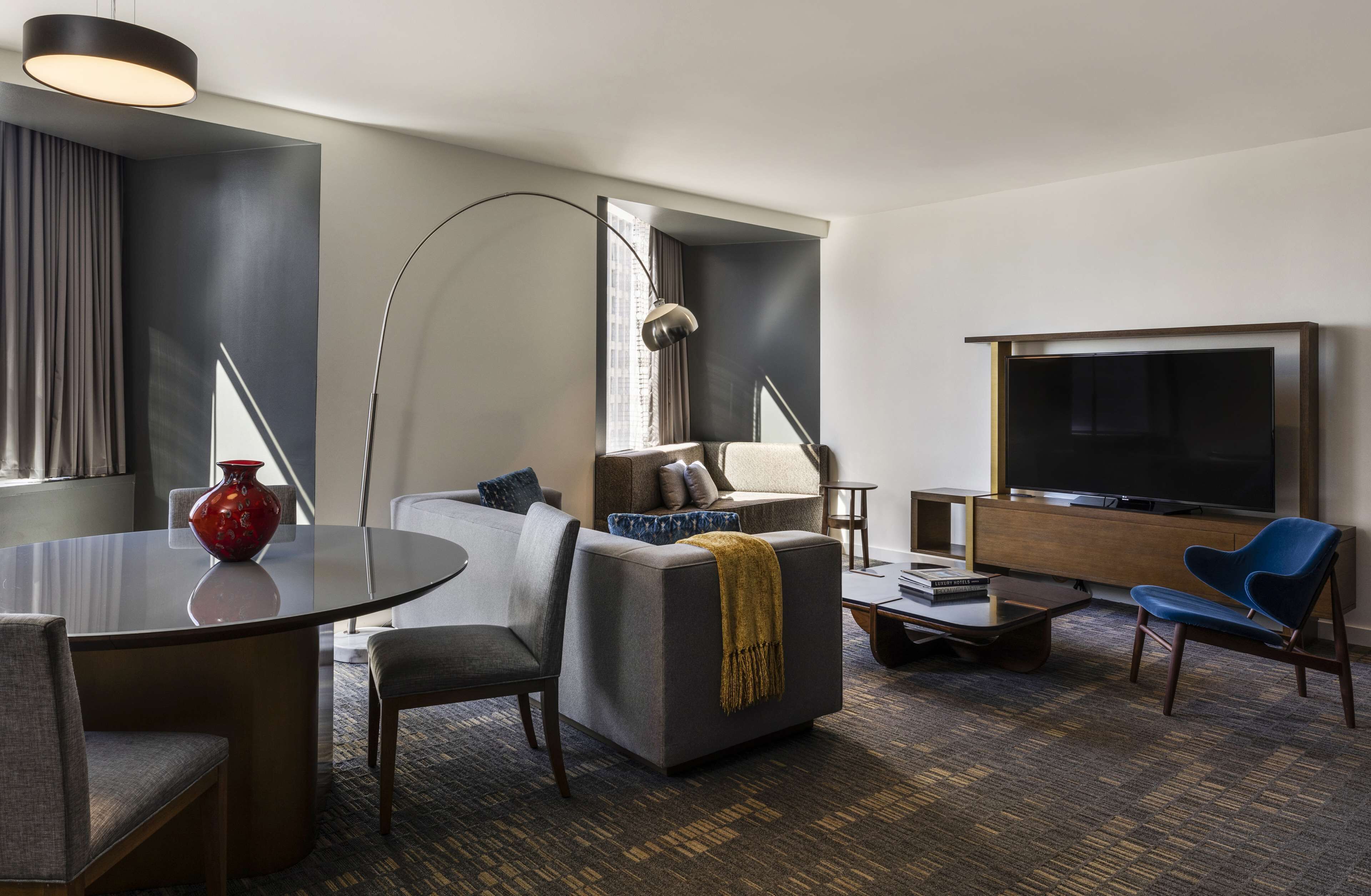 Une chambre d’hôtel moderne avec une table à manger ronde, un canapé, un téléviseur et une grande fenêtre.