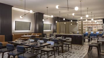 Un restaurant moderne avec des tables hautes et des banquettes, un bar bien garni avec une variété de bouteilles d’alcool, et un éclairage suspendu.