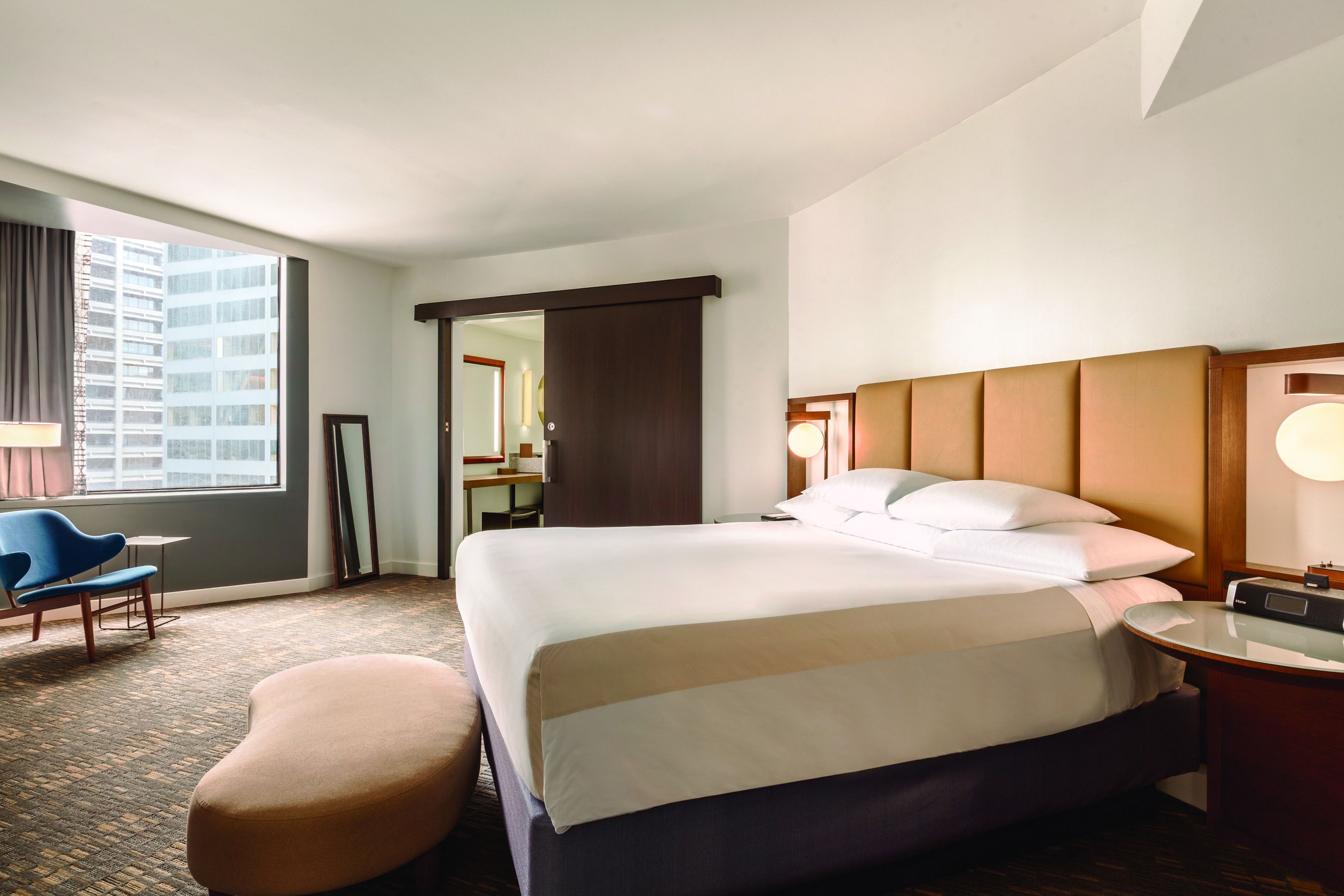 Habitación de hotel con una cama grande, un escritorio, una silla y vistas a un paisaje urbano.