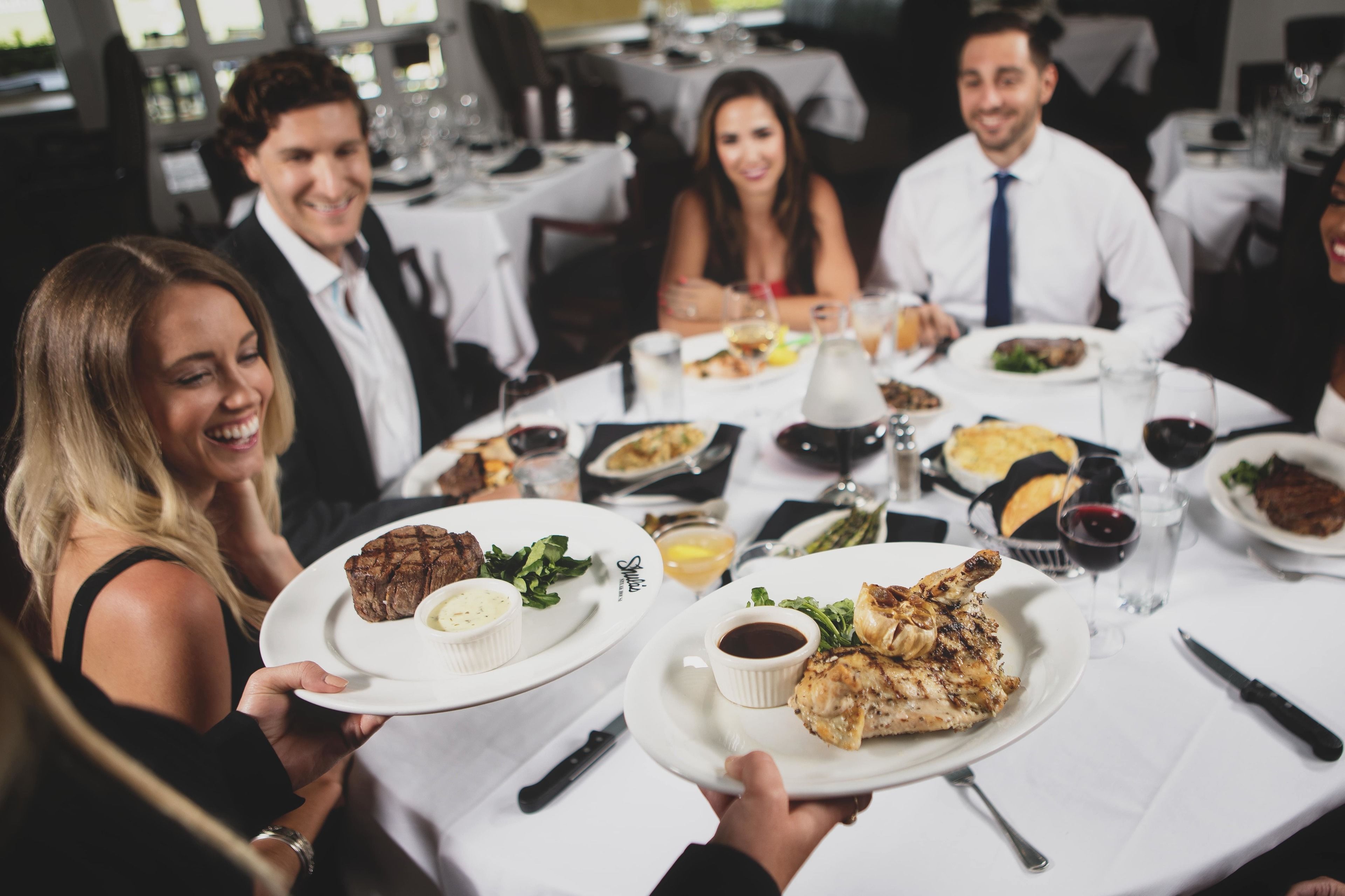 A group of people dining at a restaurant with multiple dishes on the table, including a chicken dish and a steak.