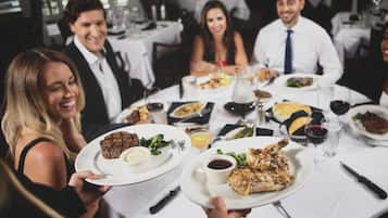 A group of people dining at a restaurant with multiple dishes on the table, including a chicken dish and a steak.