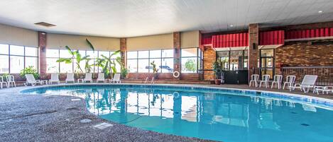 An indoor swimming pool with lounge chairs and a brick wall.