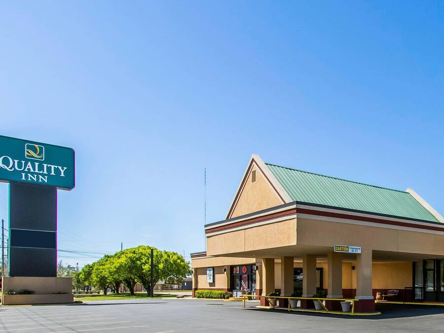 A Quality Inn with a prominent sign, a covered outdoor seating area, and a clear sky.