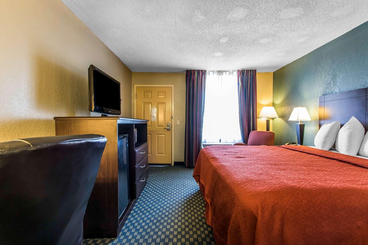 A hotel room with a bed, a desk, a television, and a door.