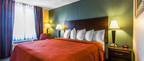A hotel room with a large bed, two bedside lamps, a chair, and a nightstand.
