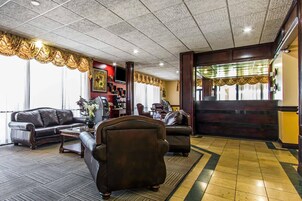 Um hall com sofás de couro, balcão de recepção, escada e tapete estampado.