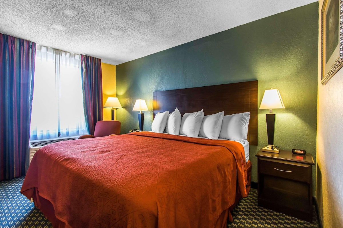 A hotel room with a large bed, two bedside lamps, a chair, and a nightstand.