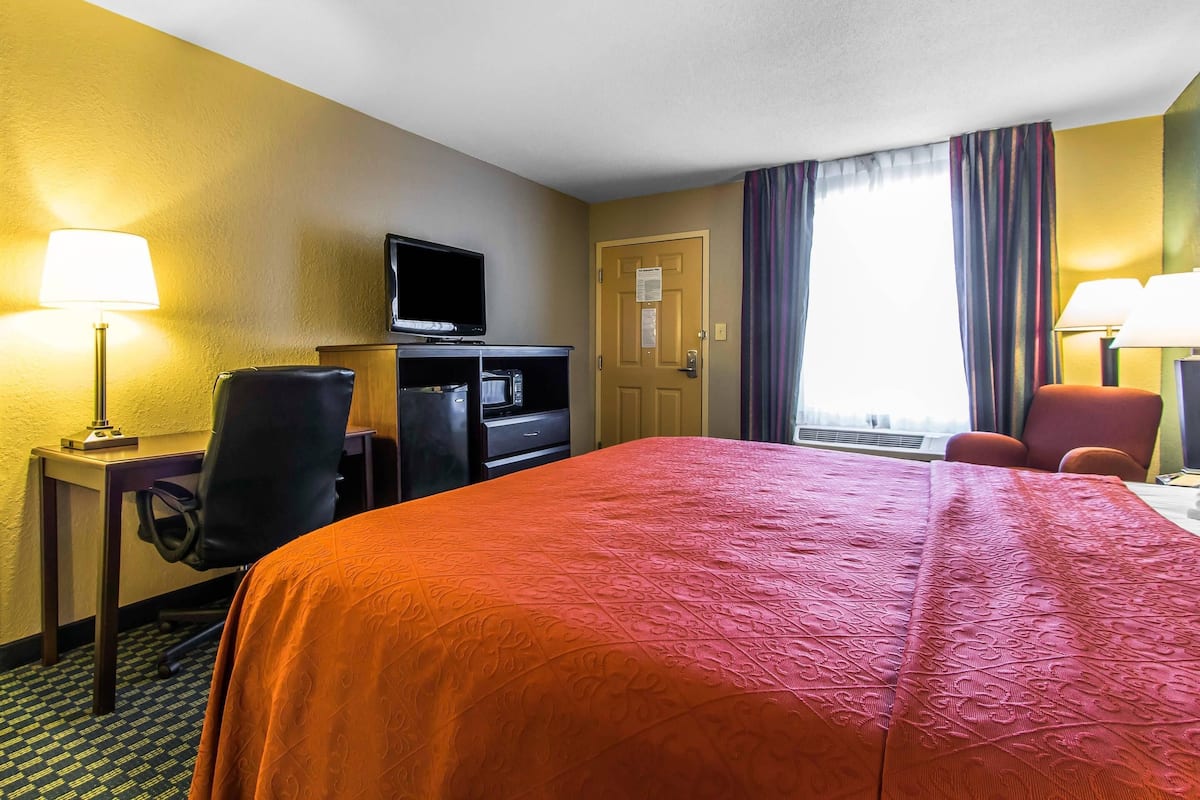 A hotel room with a bed, desk, chair, television, and a door with a window.