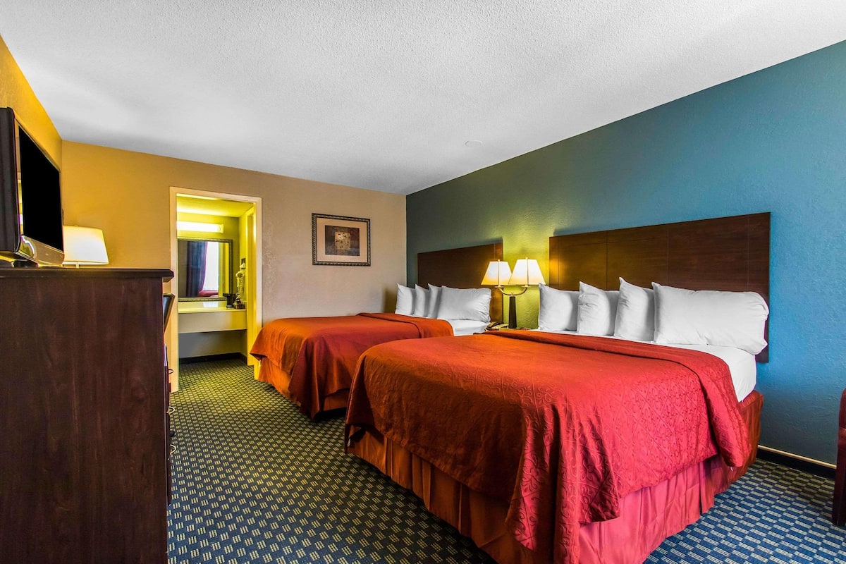 A hotel room with two beds, a desk, a TV, and a bathroom visible through an open door.