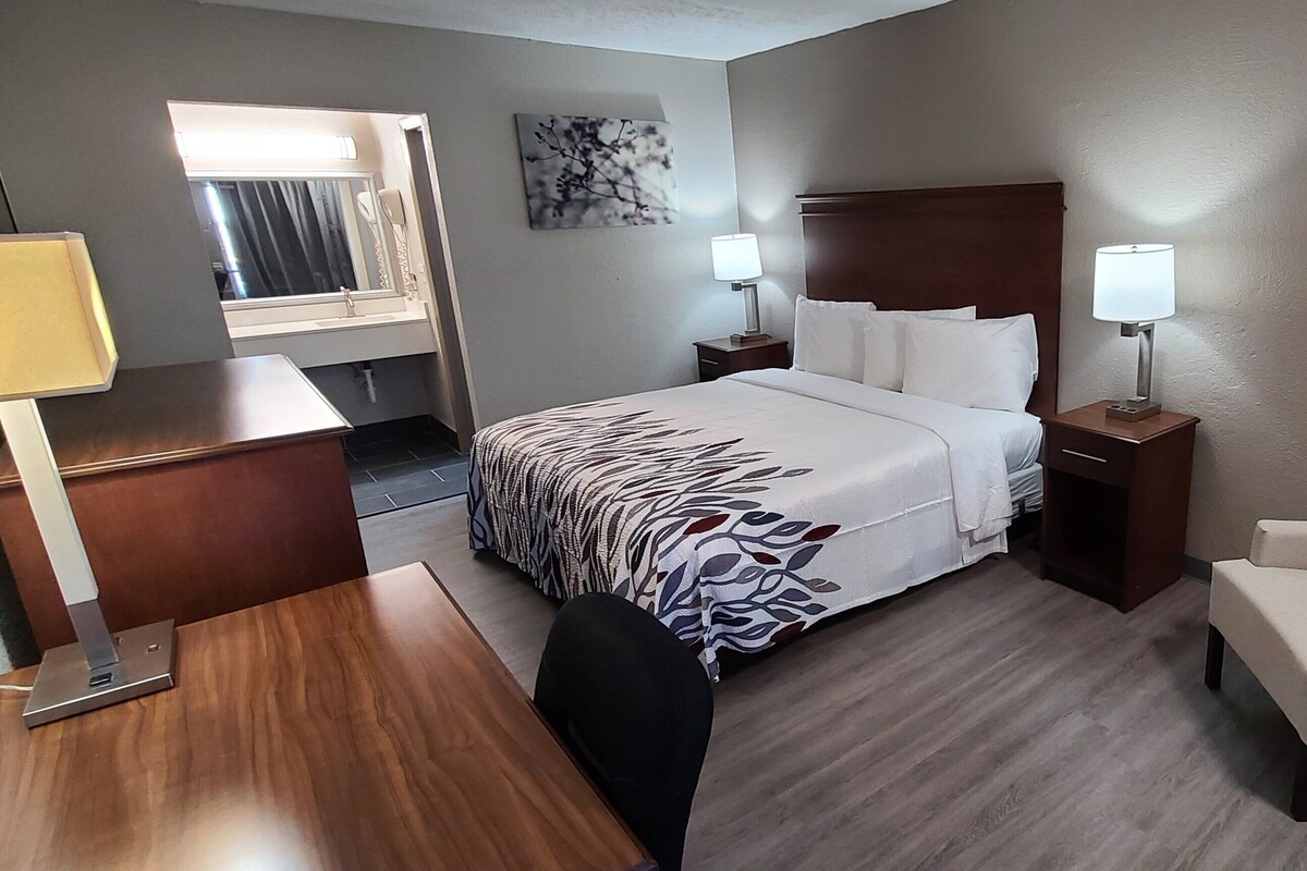 A hotel room with a bed, bedside tables with lamps, a desk, a chair, and a sofa.