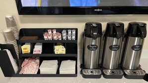 Ein Kaffee-Bereich mit Kaffeemaschine, Wasserspender und einer Ablage für Kaffeekapseln und Servietten.